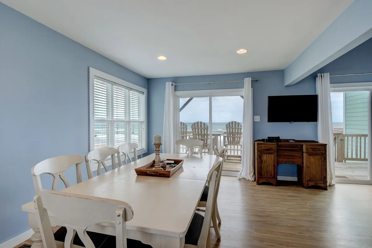 A cozy dining area with a table overlooking a window that opens to a sea view and an outdoor seating area. The space is ideal for family meals, game nights, or quiet moments appreciating the scenery.