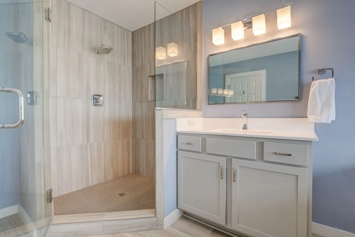 A bright bathroom with a glass shower enclosure, a vanity with a sink and mirror, and stylish light fixtures. The space is airy and calming, ideal for freshening up after a day at the beach.
